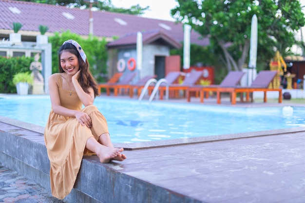 Asian woman in a brown dress Relax feel happy. With tourism At the pool