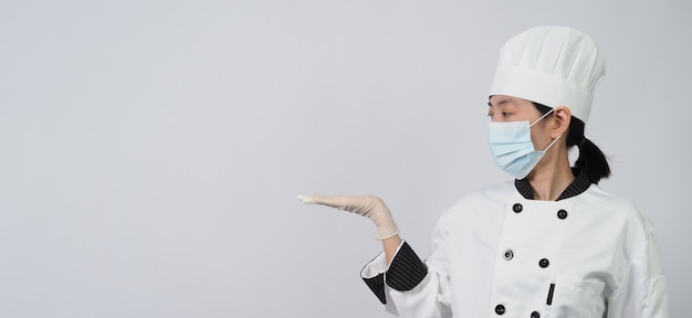 Asian woman chef in white color uniform with hygienic such as medical face mask and rubber hand glove for prevent or protect covid-19 or coronavirus pandemic.