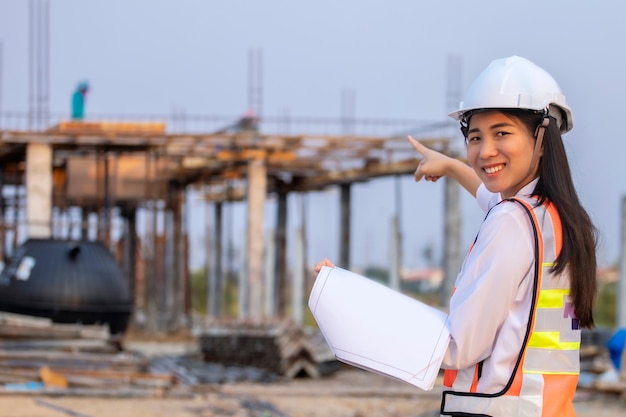 Asian woman civil engineer paper plan building architect wearing white safety helmet