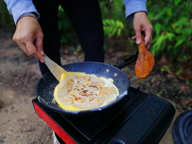 Asian woman cooking roti canai at forest during outdoor camping