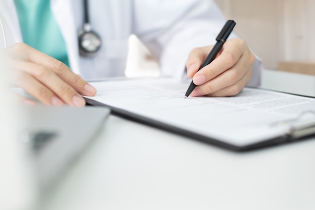 Asian woman Doctor with green cloth and lab coat working and taking note information on a clipboard.