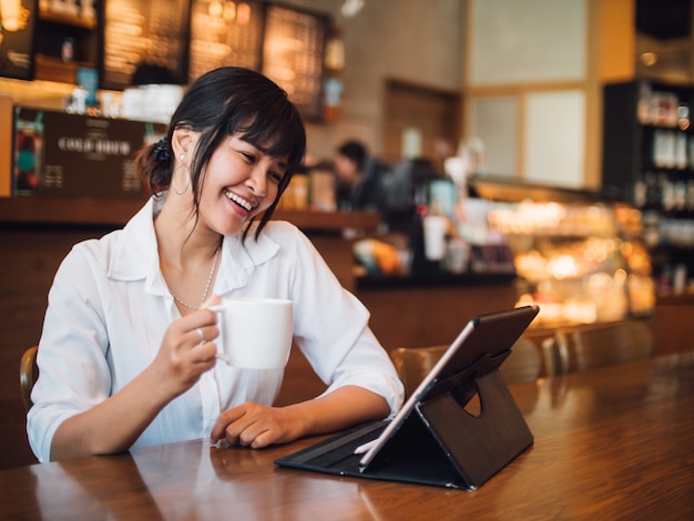 Asian woman drinking coffee in cafe and using laptop computer for working business