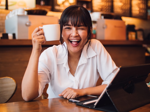 Asian woman drinking coffee in cafe and using laptop computer for working business