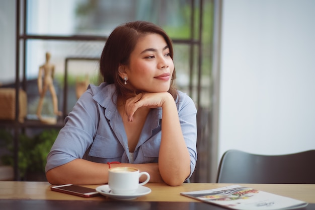 Asian woman drinking coffee in coffee shop cafe and using mobile phone