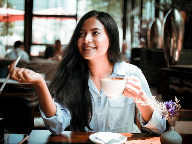 Asian woman drinking coffee and working with laptop computer in cafe