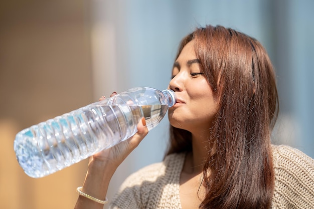 Asian Woman drinks big bottle water in outdoor green bokeh tree background