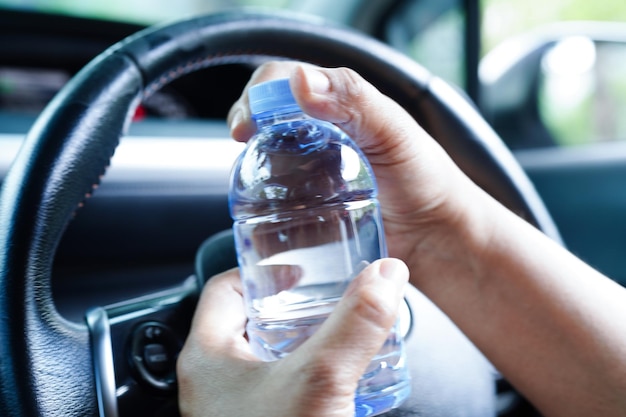 Asian woman driver hold cold water for drink in car dangerous and risk an accident