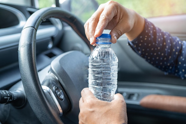 Asian woman driver holding bottle for drink water while driving a car Plastic hot water bottle cause fire