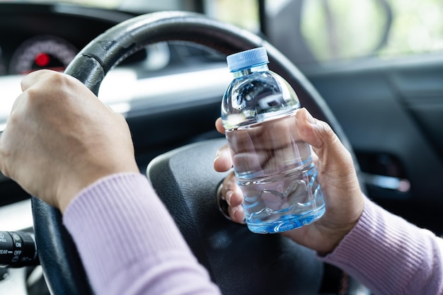 Asian woman driver holding bottle for drink water while driving a car Plastic hot water bottle cause fire