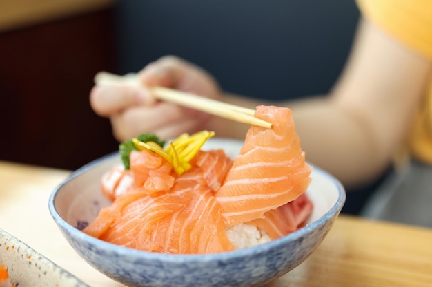 Asian woman eating salmon slice sashimi with rice in Japanese restaurant