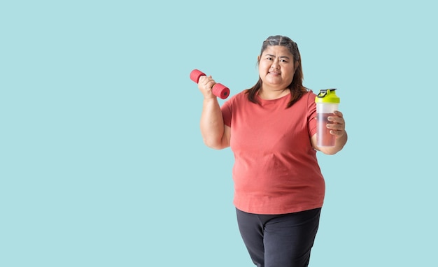 Asian woman fat holding dumbbell and a water or supplement bottle isolated on blue background