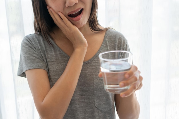 Asian woman feeling teeth pain Closeup of sad girl suffering from toothache after drinking water Dental health and care teeth problem concept Copy space