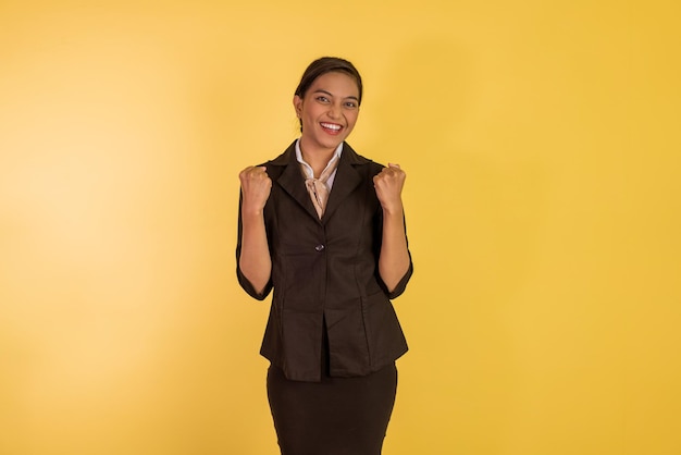 Asian woman in formal outfit standing with clenched arms and smiling on orange isolated background