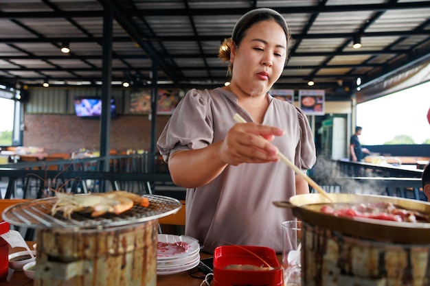 Asian woman grill food on grille charcoal stove at grilled restaurant