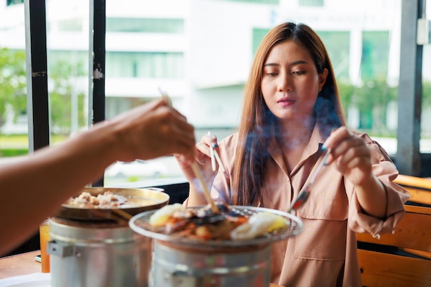 Asian woman grill food on grille charcoal stove with her boyfriend at grilled restaurant