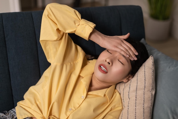 Asian Woman Having Headache And Fever Lying On Sofa Indoor