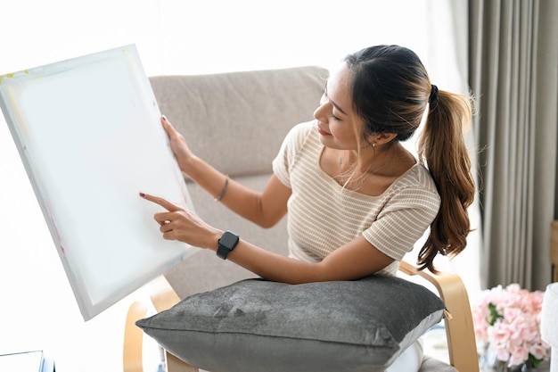 An Asian woman holding a blank canvas looking at a canvas or showing her picture on a canvas