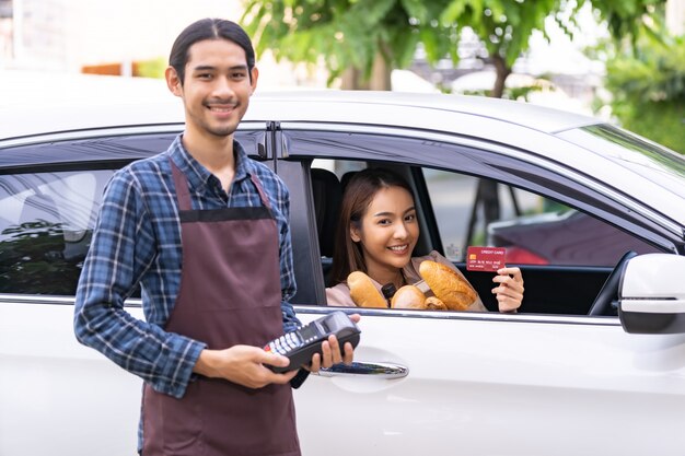 Asian woman holding a credit card and paying from the car