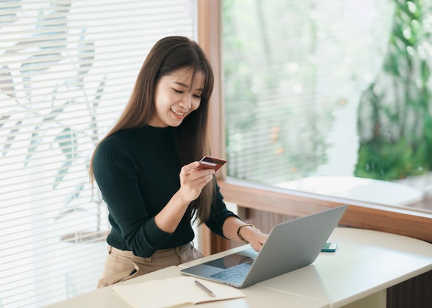 Asian woman holding credit card and using laptop computer Businesswoman working at home Online shopping ecommerce internet banking spending money working from home concept