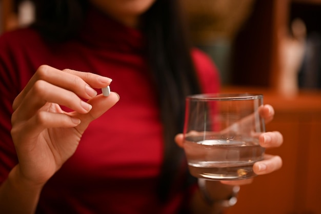 Asian woman holding a glass of water and a vitamin or medicine tablet. cropped and closeup image