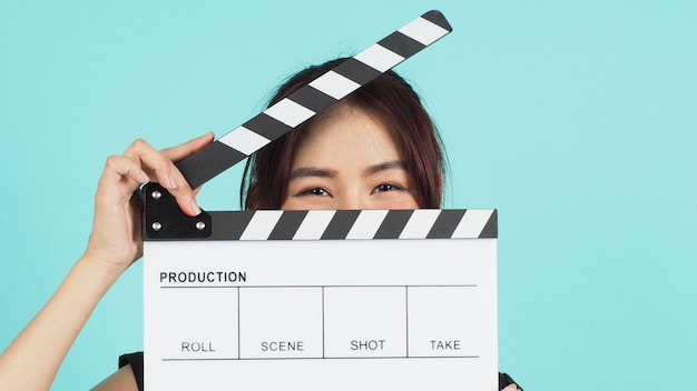 Asian Woman holding whiteclapperboard and closing her face on mint or Tiffany Blue background.