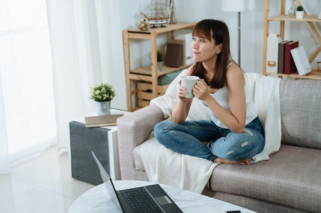 asian woman is holding a mug and taking a break on a holiday morning. pretty lady is looking out the window enjoying her tea and the refreshing morning.