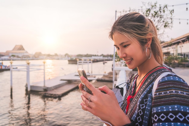 Asian woman is using mobile while traveling in Bangkok Chao Phraya river at sunset