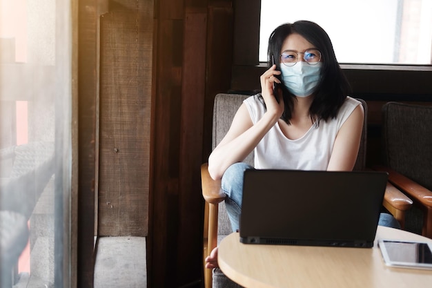 Asian woman is wearing mask for prevent covid19 and calling on smartphone and online working