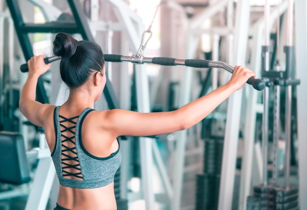 Asian woman is working out her back rear muscle by pulling weight in fitness sport gym