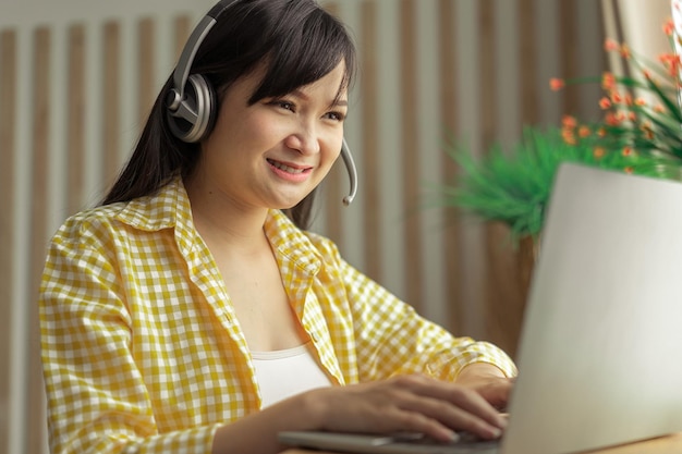 Asian woman in jeans and plaid shirt Portrait of a young happy female sitting on the couch and working or studying online