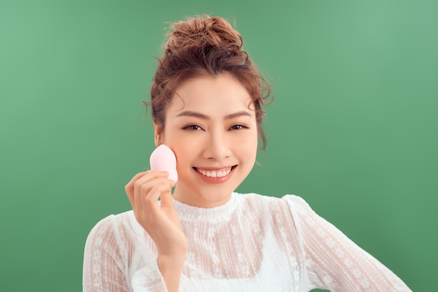 Asian woman laughing and holding facial sponge isolated over green background