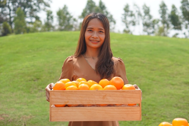 Asian woman lifting a basket of oranges in a field