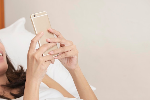 Asian woman lying down while using a mobile phone on the bed