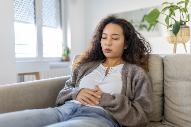 Asian woman lying on sofa looking sick in the living room Beautiful young woman lying on bed and holding hands on her stomach Woman having painful stomachache on bed Menstrual period