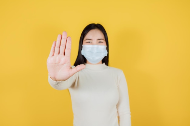 Asian woman in medical face mask to protect Covid19 show stop hands gesture for stop corona virus outbreak on yellow background