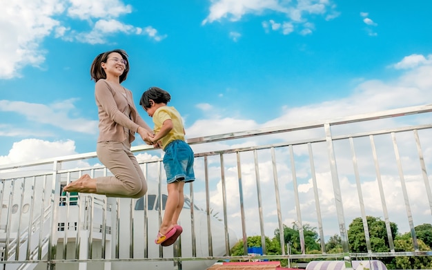 Asian woman mother with little child girl jumping with a plane and blue sky background, happy family relaxes time concept.