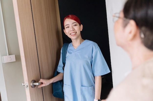 Asian woman nurse wearing scrubs home caregiver visit senior Asian woman at the entrance with a smile Home health care and nursing home concept