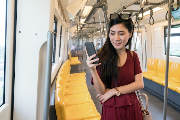 Asian woman passenger using the social network via smart mobile phone in the Skytrain rails