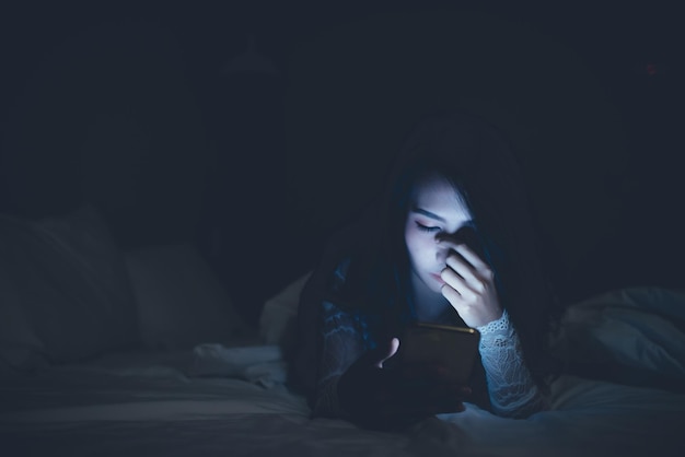 Asian woman playing game on smartphone in the bed at nightThailand peopleAddict social media