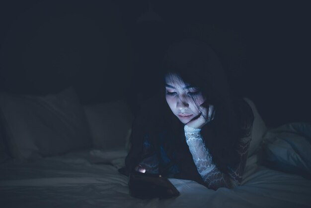 Asian woman playing game on smartphone in the bed at nightThailand peopleAddict social media