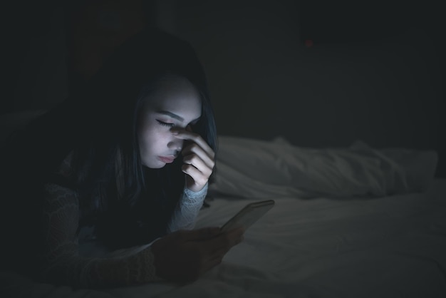 Asian woman playing game on smartphone in the bed at nightThailand peopleAddict social media