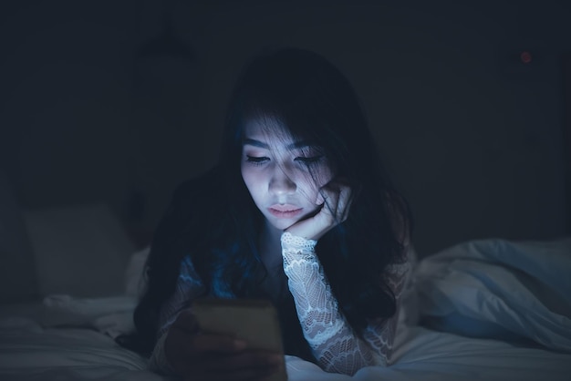 Asian woman playing game on smartphone in the bed at nightThailand peopleAddict social media