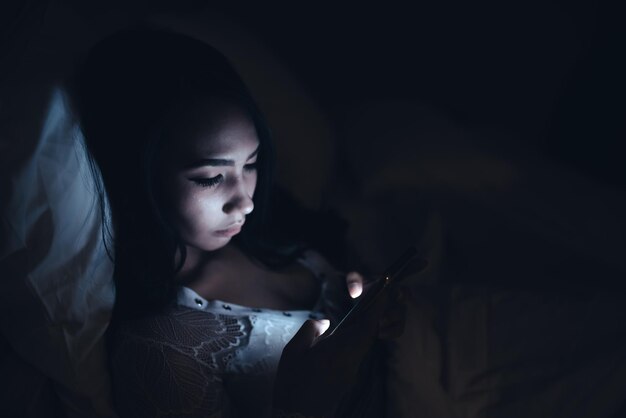 Asian woman playing game on smartphone in the bed at nightThailand peopleAddict social media