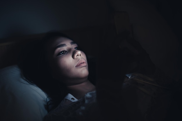 Asian woman playing game on smartphone in the bed at nightThailand peopleAddict social media