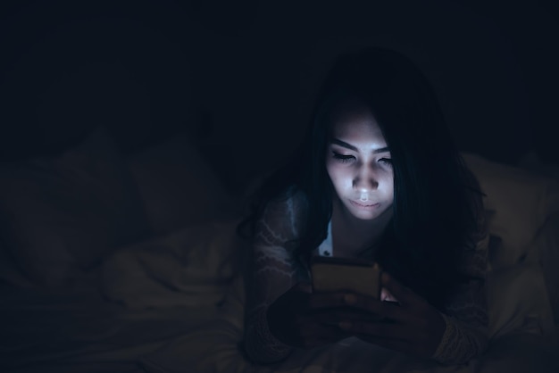 Asian woman playing game on smartphone in the bed at nightThailand peopleAddict social media