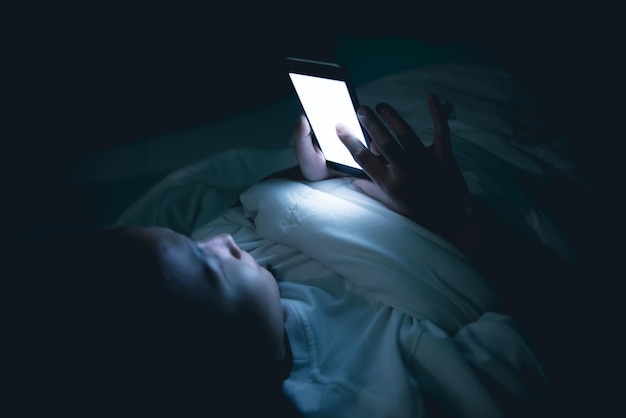 Asian woman playing game on smartphone in the bed at nightThailand peopleAddict social media