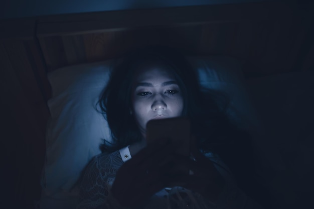 Asian woman playing game on smartphone in the bed at nightThailand peopleAddict social media