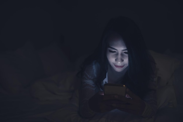 Asian woman playing game on smartphone in the bed at nightThailand peopleAddict social media