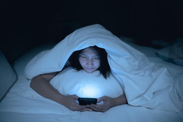 Asian woman playing game on smartphone in the bed at nightThailand peopleAddict social media