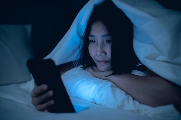 Asian woman playing game on smartphone in the bed at nightThailand peopleAddict social media